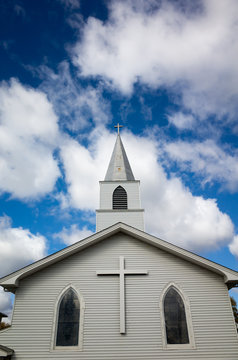 white church with cross outside verticle view with blue sky with white puffy clouds