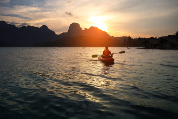 Silhouette scenery during sunset with a man paddling the kayak at natural attractions in Ratchaprapha Dam,Khao Sok National Park,SuratThani Province in Thailand. Traveling and recreation Concept.
