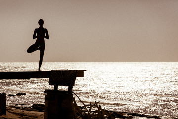 Yoga on a dock with the ocean in the background at sunset in silhouette.