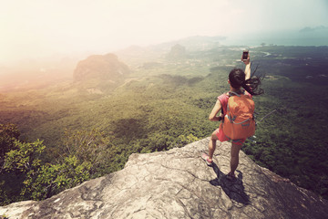young woman hiker taking photo with smartphone on mountain peak cliff