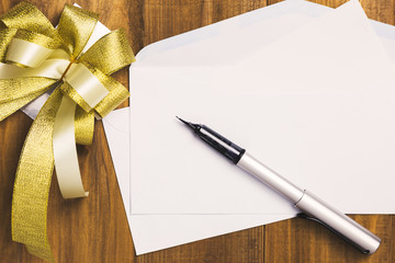 Luxury pen and blank white card with golden ribbon on wood background