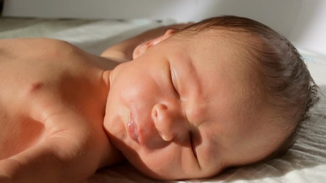 Closeup shot of crying newborn baby lying on bed in sun rays