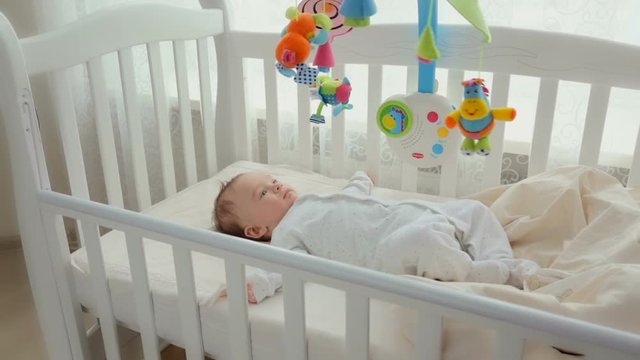 Cute baby lying in cradle with spinning toy carousel