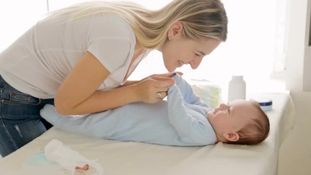 Beautiful young mother undressing her baby son lying on changing table