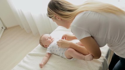 Beautiful young mother undressing her 3 months old baby boy lying on changing table