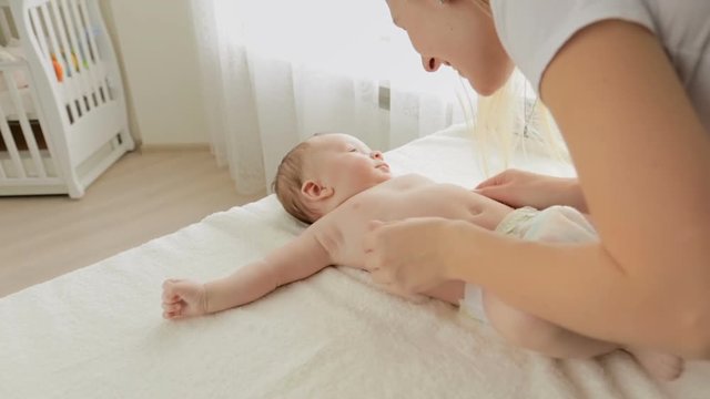 Closeup shot of young mother undressing her baby boy and tickling him on changing table