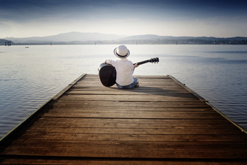boy sitting on a pier and playing a guitar 