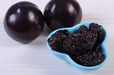 Fresh and dried plums in blue bowl on wooden table, healthy food