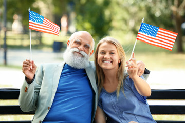 Granddaughter and her grandfather with American flags in a park