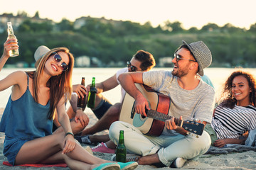 Group of friends listening to guitar and drinking beer the beach