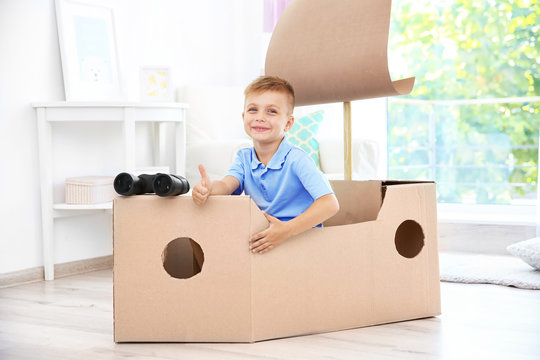 Little boy playing with cardboard ship indoors