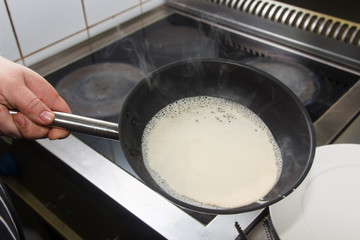 Cooking pancakes the cook pours the batter in the pan.
