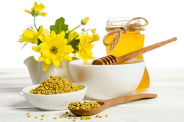 the jar of honey near two bowls, one with  of pollen another wit