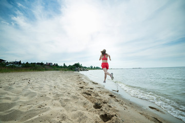 Young lady running. Woman runner running at the sunny summer sand beach. Workout near ocean sea coast. Beautiful fit girl. Fitness model caucasian ethnicity outdoors. Weight loss exercise. Jogging.