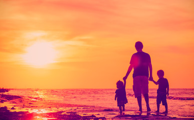 father and two kids walking on beach at sunset