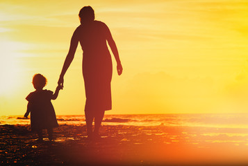 Fototapeta na wymiar mother and little daughter walking on beach at sunset