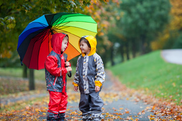 Two adorable children, boy brothers, playing in park with umbrel