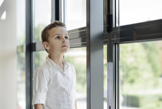 beautiful boy standing next to a window high-rise building 