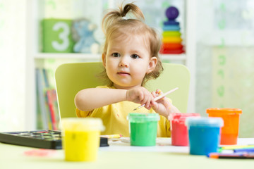 Cute little child painting with paintbrush and colorful paints