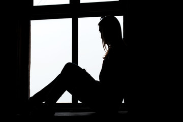 Woman looking through window sitting on the window sill