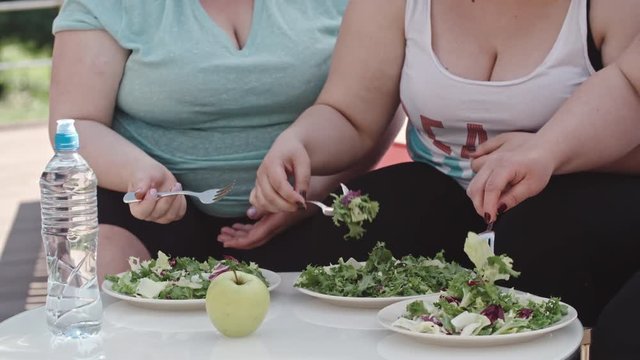 Midsection of three obese women sitting at the table outdoor and eating lettuce salad