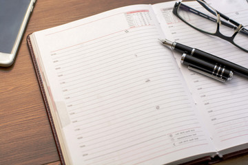 Notebook with glasses, pen and smart phone on wooden background.