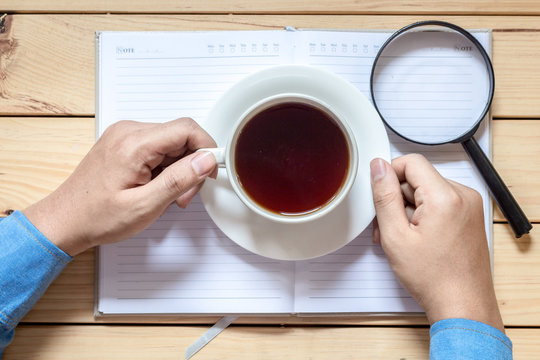 Hands with cup of coffee with notebook on wooden table