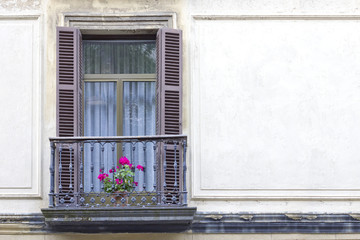 Fototapeta na wymiar Old window with opened brown shutters and an lonely flower pot with geranium flowers.