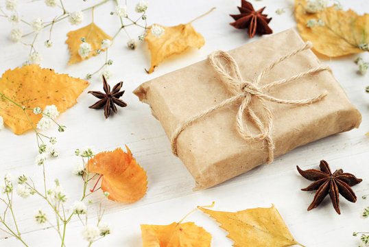 Autumn eco-craft. Handmade gift paper wrapping, dried fall leaves decor arrangement, light background.