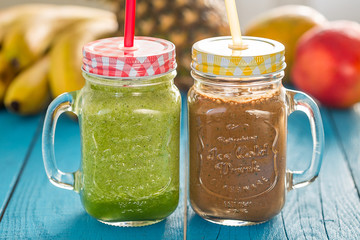 Healthy Green and Chocolate Smoothie in the Glass Jars with Fruits on the Background