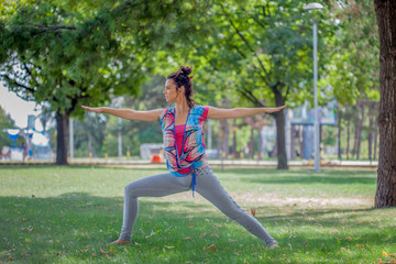 Young woman practicing yoga in the park on the green grass with