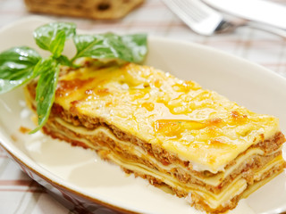 Traditional lasagna made with minced beef bolognese sauce topped with basil leafs served on a white plate