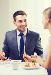 smiling couple eating sushi at restaurant