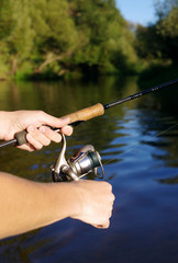 Fishing with a spinning on the river. Man catches fish, a close up of a hand and the spinning reel.
