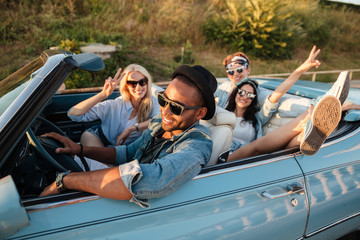 Smiling friends driving car and showing peace sign in summer