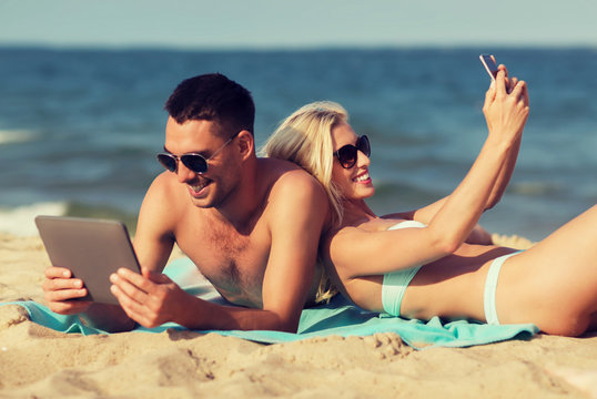 happy couple with modern gadgets lying on beach