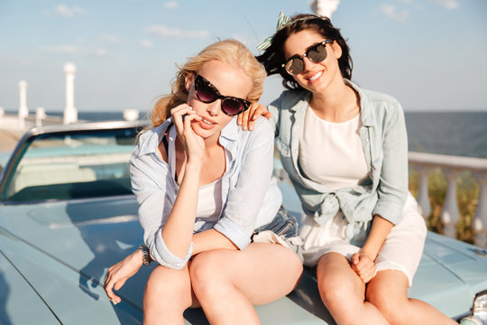 Two women sitting on the car hood together