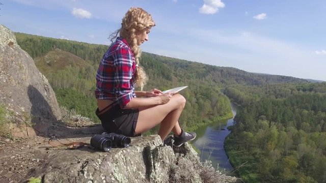 Young blonde woman tourist  on a cliff over river Berd studying a map and view the neighborhood. Russia, Siberia, Salair