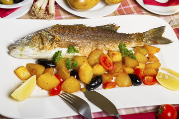 Fried seabass with side dish on a plate, served on a table.