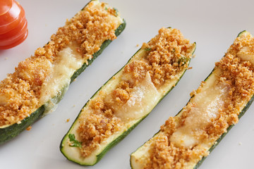 stuffed courgette on a white sqare plate in a rustic enviroment.