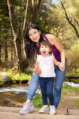 Fototapeta premium Asian Woman with her little daughter in the woods near the river standing on a log