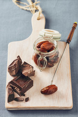 Chocolate, date fruit and cinnamon on a white chopping board on a blue table. Pastel colors