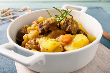 Sicilian stew in a white pot on a blue table, pastel color