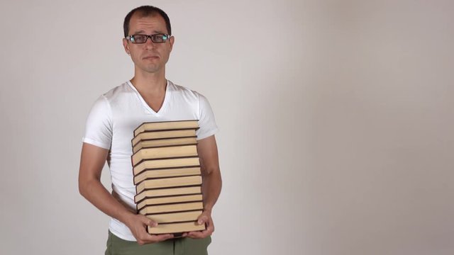 Nerdy man in black rim glasses carrying big stack of books against gray background, isolated. 4K shot