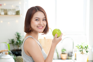 Happy Young Asian Woman Eating Green Apple on Kitchen. Diet. Die