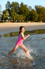 Happy young Asian girl running and jumping in the waves during summer vacation on exotic tropical beach. Kids play at the sea. 