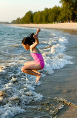 Happy young Asian girl running and jumping in the waves during summer vacation on exotic tropical beach. Kids play at the sea. 