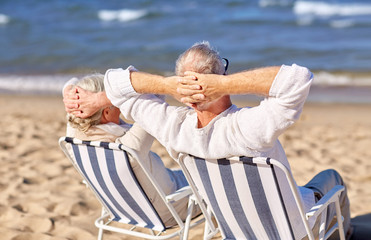 senior couple sitting on chairs at summer beach