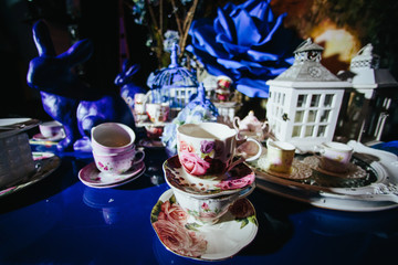 Table decor. Tea cups painted with pink flowers stand on a blue