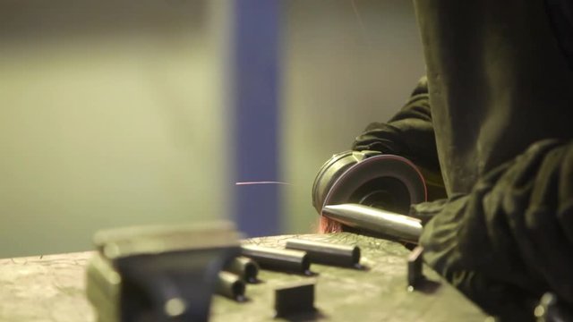 Shaky footage of a worker polishing some metal bar with a grinder, with sparks flying.